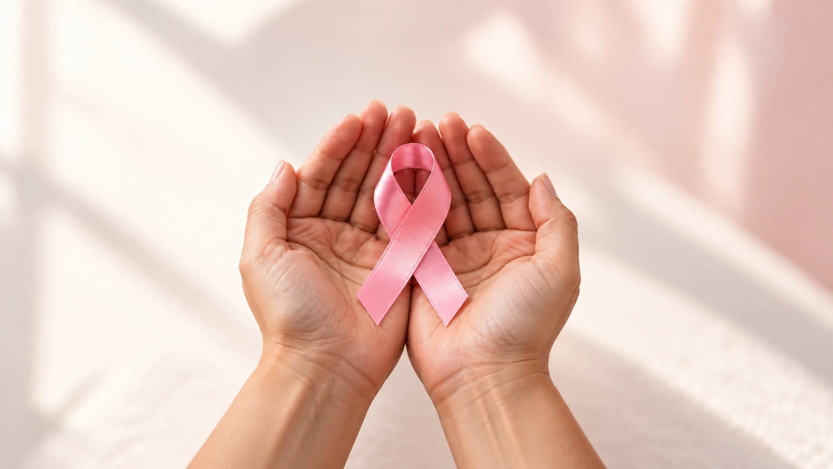 Mãos acolhem um laço rosa, símbolo da conscientização sobre o câncer de mama.